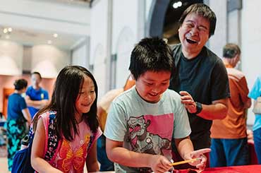 two children doing an activity with a man smiling next to them