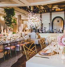 long tables in rows with gold chairs, in the center is a large pink and white floral centerpiece 