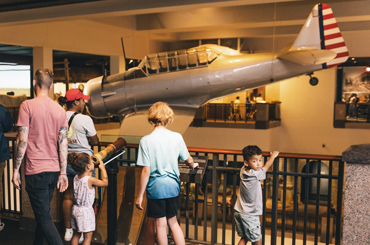Museum visitors looking at an AT-6A military airplane hanging from the ceiling inside the Bullock Museum.