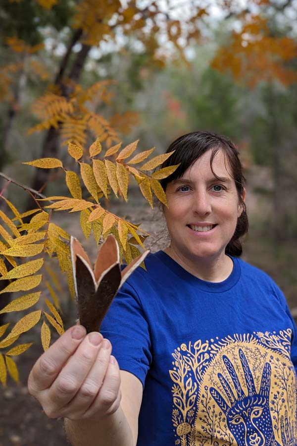 a woman holding a plant and posing for the camera while walking on a forest trail