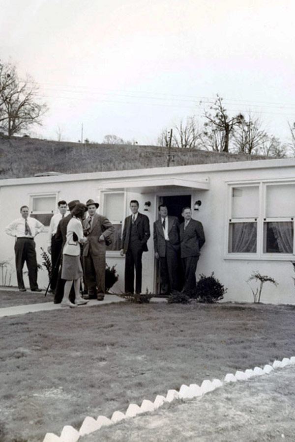 a black and white photo of a group of people in front of a one-story home