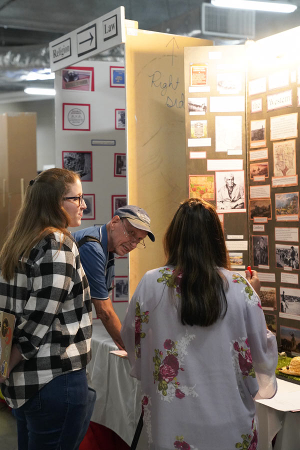 three judges looking at trifold boards of history projects 