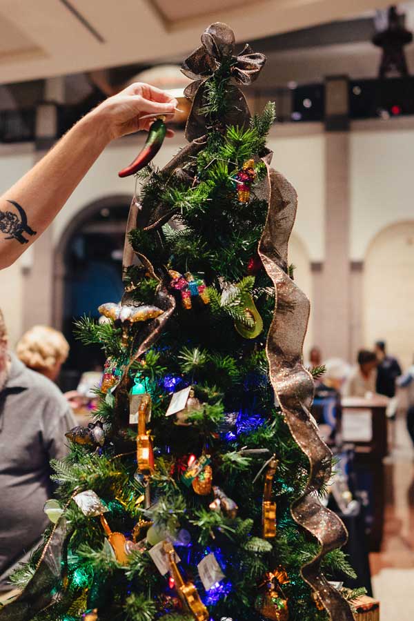 a hand placing a jalapeno ornament on a holiday tree