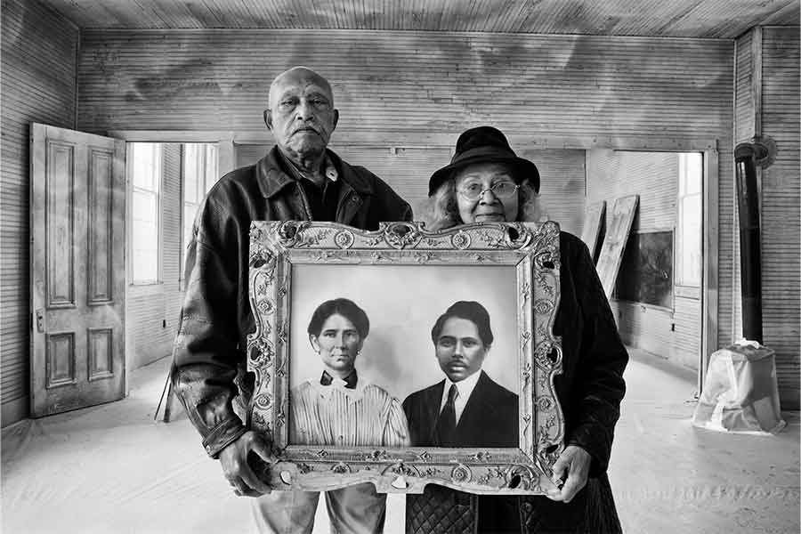 a black and white photo of a man and a woman standing in an empty schoolhouse holding a picture frame holding a painting of a man and a woman