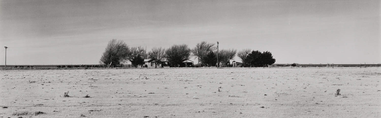 black and white photo of desolate land with some farm houses on the horizon