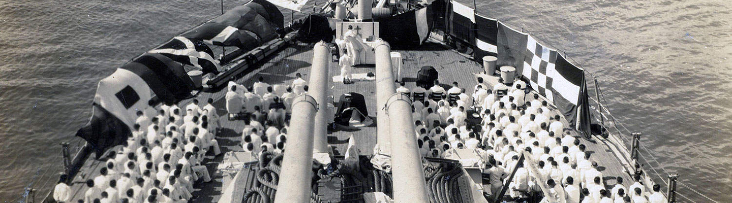 view looking down the deck of the Battleship Texas with sailors in white suits and four long gun barrels