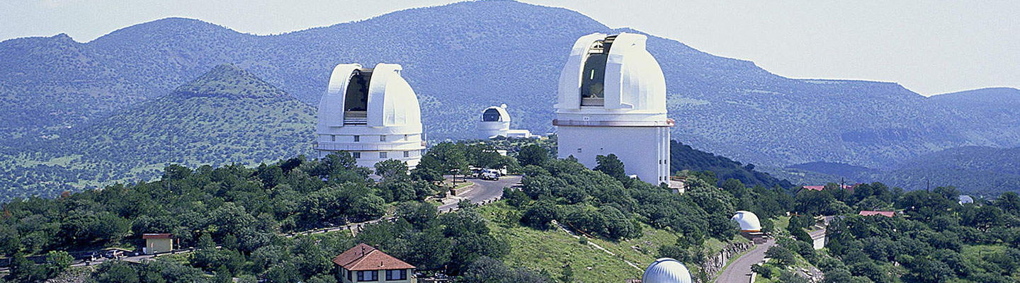 two rounded telescope buildings on a hill with mountain range in the background