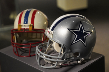 two NFL helmets, one silver with a blue star in the foreground, and one white helmet with an oil rig logo in the background