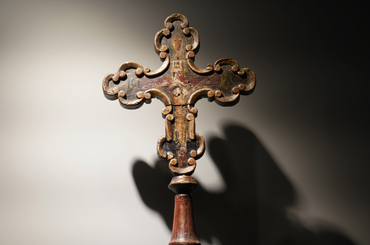 an ornate wooden Catholic cross with a painting on it, sitting in a display case at the Bullock Museum