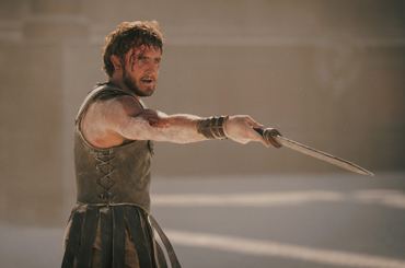 still image from "Gladiator II" of Lucius pointing his sword at someone in an arena