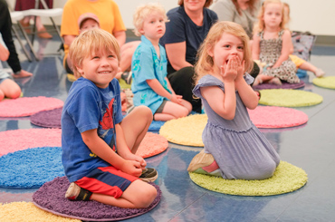 two children sitting on carpet circles smiling at an instructor